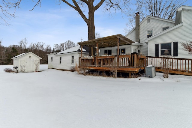 snow covered property featuring a wooden deck, a pergola, and a shed