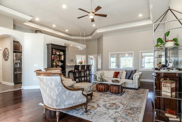 living area with crown molding, a raised ceiling, dark wood-type flooring, and arched walkways