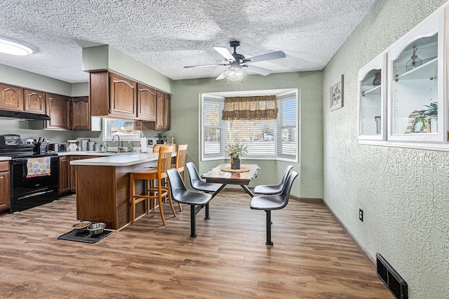 kitchen with hardwood / wood-style floors, sink, a kitchen bar, ceiling fan, and black range with electric stovetop