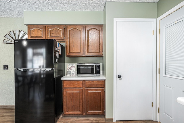 kitchen with black refrigerator, hardwood / wood-style flooring, and a textured ceiling