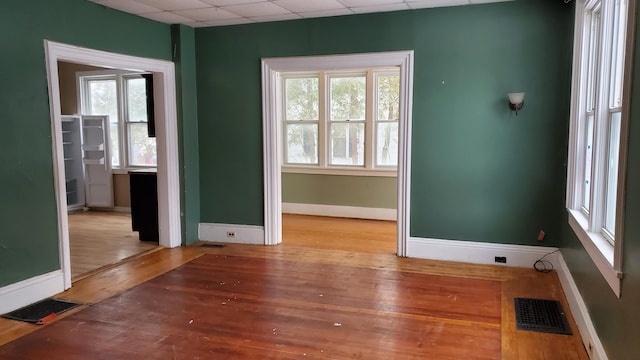 spare room featuring hardwood / wood-style flooring, a paneled ceiling, and a healthy amount of sunlight