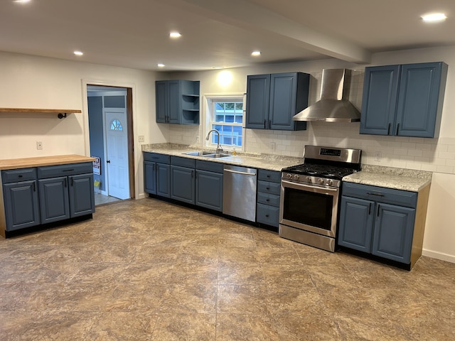 kitchen featuring wall chimney range hood, sink, appliances with stainless steel finishes, backsplash, and blue cabinets