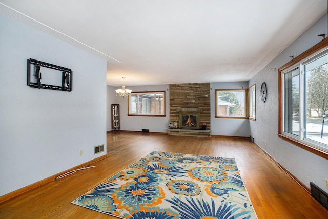 unfurnished living room with a notable chandelier, hardwood / wood-style flooring, a fireplace, and a healthy amount of sunlight