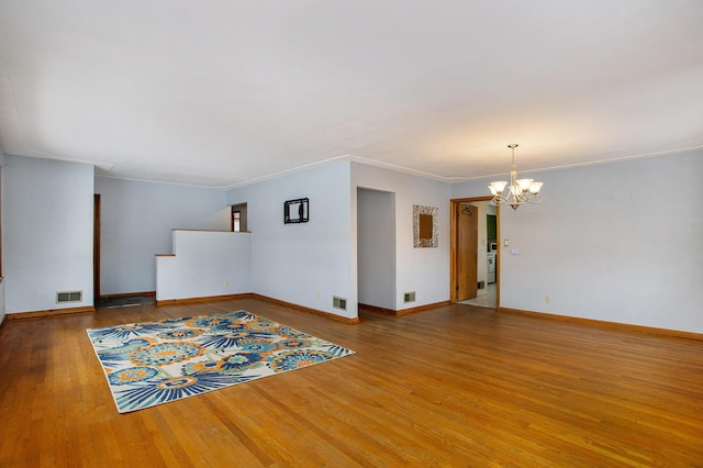 spare room featuring an inviting chandelier, ornamental molding, and wood-type flooring