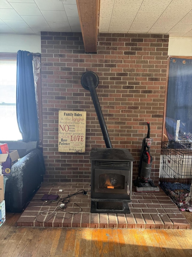 room details with beamed ceiling, hardwood / wood-style floors, and a wood stove