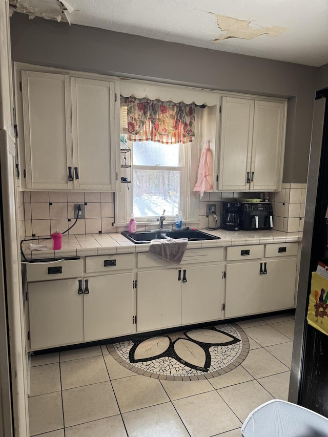 kitchen with tile countertops, white cabinetry, light tile patterned floors, and decorative backsplash