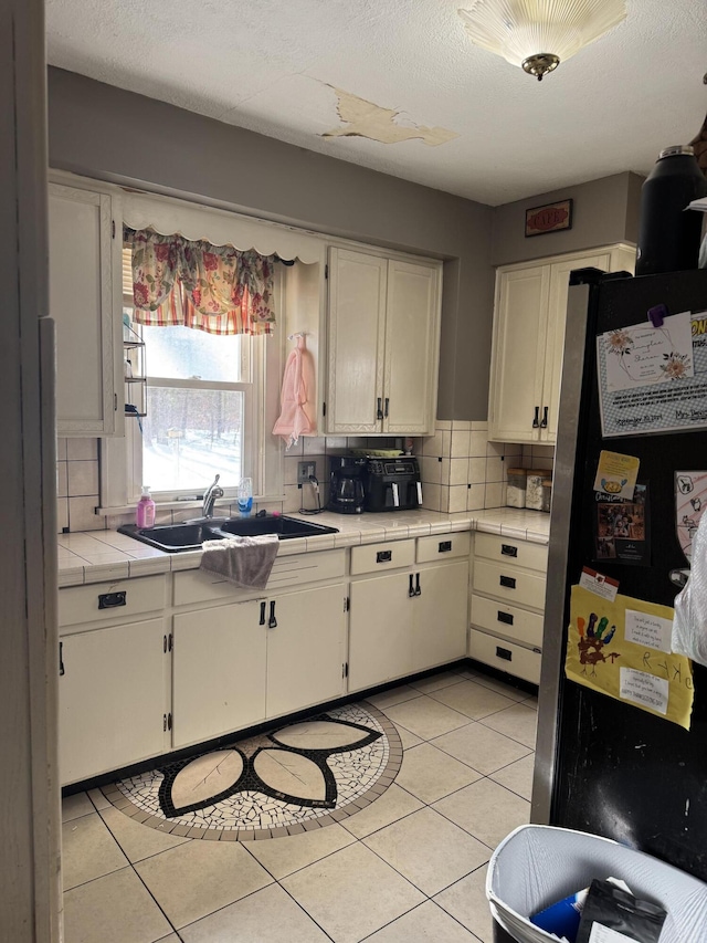 kitchen featuring sink, stainless steel refrigerator, backsplash, white cabinets, and tile countertops