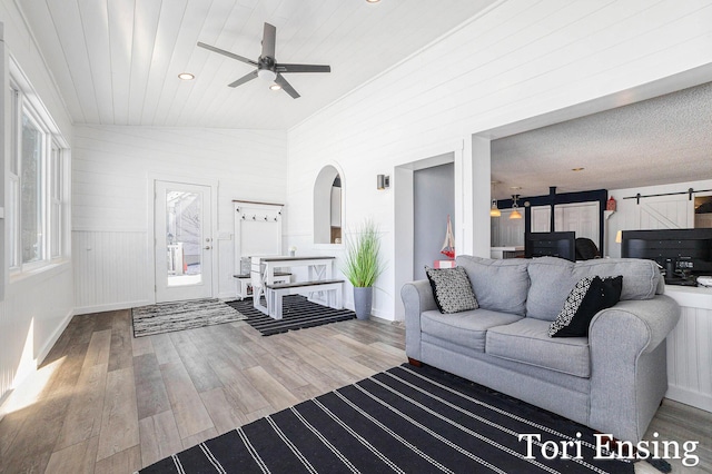 living room featuring vaulted ceiling, wood-type flooring, a barn door, and ceiling fan