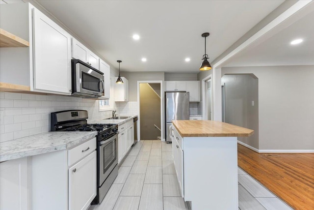 kitchen featuring pendant lighting, sink, appliances with stainless steel finishes, white cabinetry, and a center island