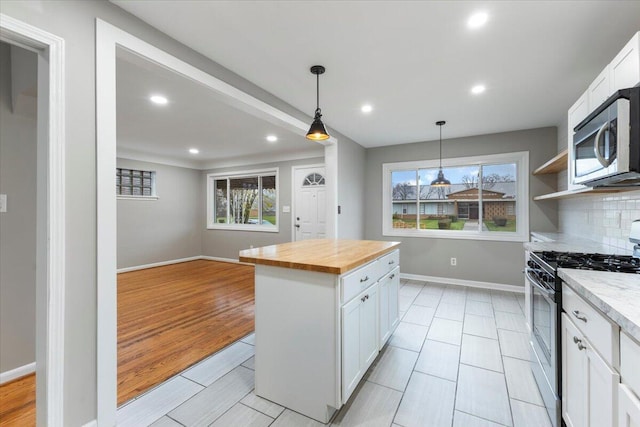 kitchen featuring butcher block countertops, white cabinetry, hanging light fixtures, appliances with stainless steel finishes, and backsplash