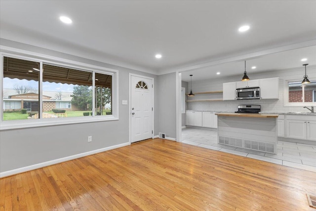 kitchen featuring sink, white cabinetry, light wood-type flooring, stainless steel appliances, and decorative backsplash