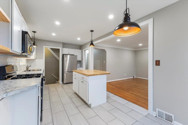 kitchen with white cabinetry, stainless steel appliances, a center island, and wooden counters