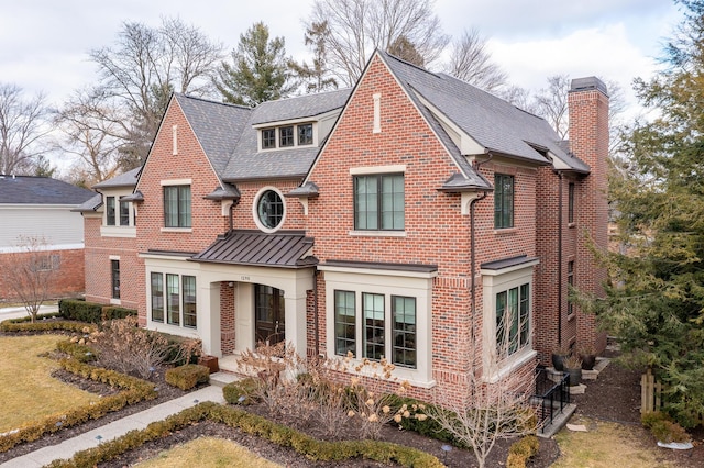 view of front of home featuring a standing seam roof, brick siding, metal roof, and a chimney