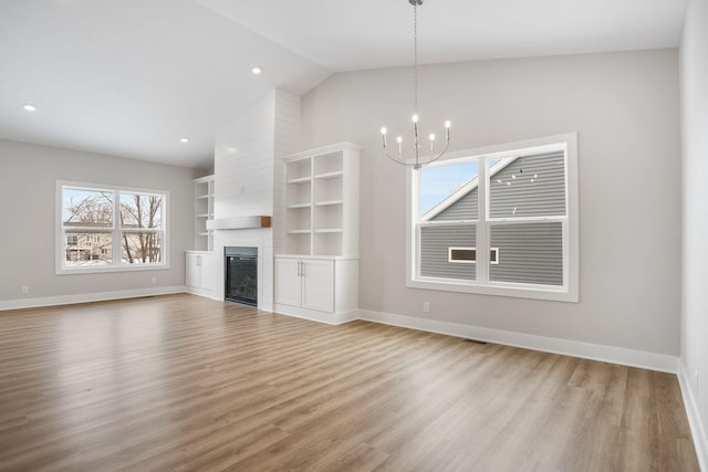 unfurnished living room featuring a large fireplace, lofted ceiling, light hardwood / wood-style floors, and a notable chandelier