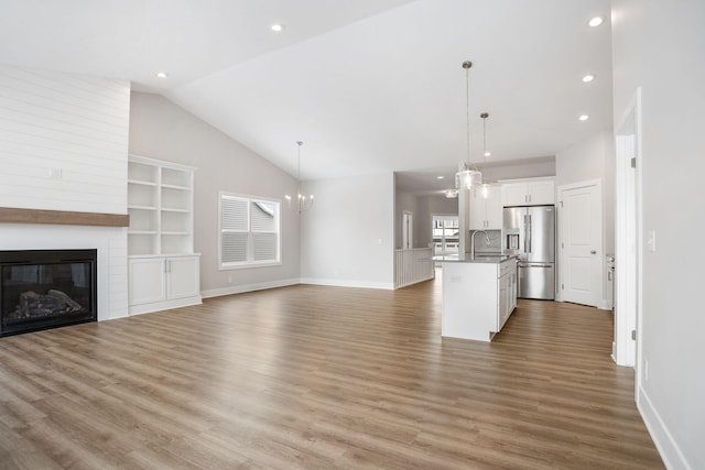 unfurnished living room with a fireplace, light hardwood / wood-style floors, built in shelves, vaulted ceiling, and a chandelier