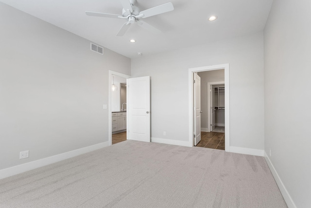 unfurnished bedroom with dark carpet, a spacious closet, a closet, and ceiling fan