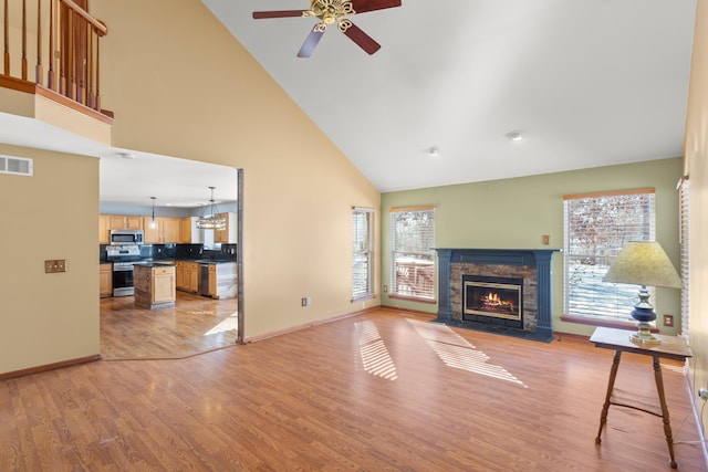 living room with ceiling fan, a stone fireplace, high vaulted ceiling, and light hardwood / wood-style flooring