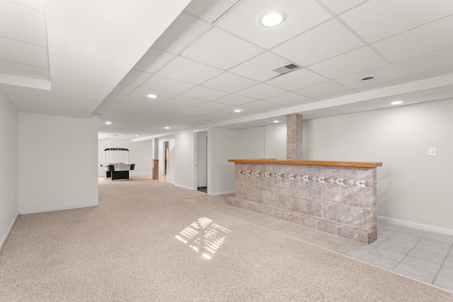 basement featuring a paneled ceiling, bar, and light colored carpet