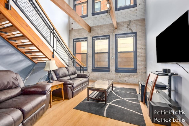 living room featuring brick wall, light hardwood / wood-style flooring, a healthy amount of sunlight, and a high ceiling