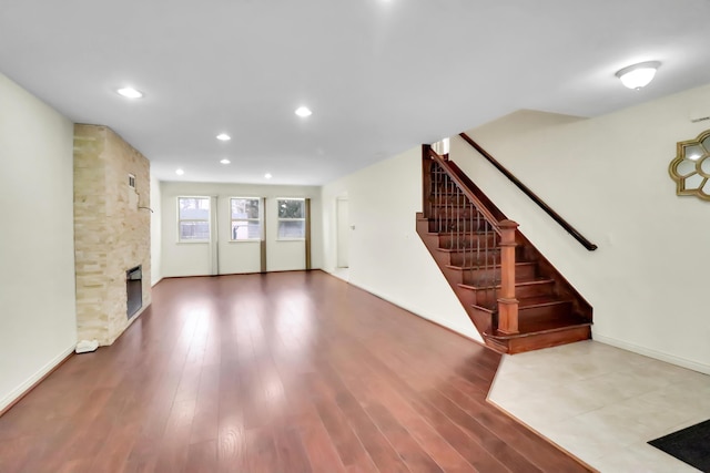 unfurnished living room with recessed lighting, wood finished floors, baseboards, a fireplace, and stairs