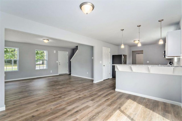 kitchen with stainless steel refrigerator, decorative light fixtures, white cabinetry, light stone countertops, and dark wood-type flooring