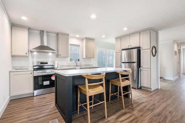 kitchen with a kitchen bar, wall chimney exhaust hood, sink, a center island, and stainless steel appliances