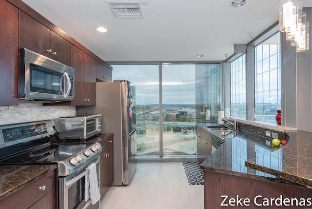 kitchen with sink, tasteful backsplash, dark stone countertops, appliances with stainless steel finishes, and pendant lighting