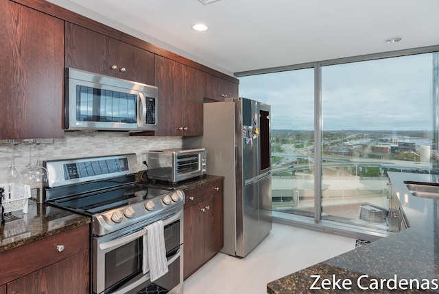 kitchen featuring sink, dark stone countertops, decorative backsplash, stainless steel appliances, and floor to ceiling windows