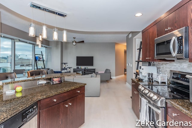 kitchen featuring appliances with stainless steel finishes, pendant lighting, tasteful backsplash, dark stone counters, and ceiling fan