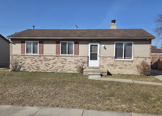 ranch-style home with entry steps, a front yard, a shingled roof, brick siding, and a chimney