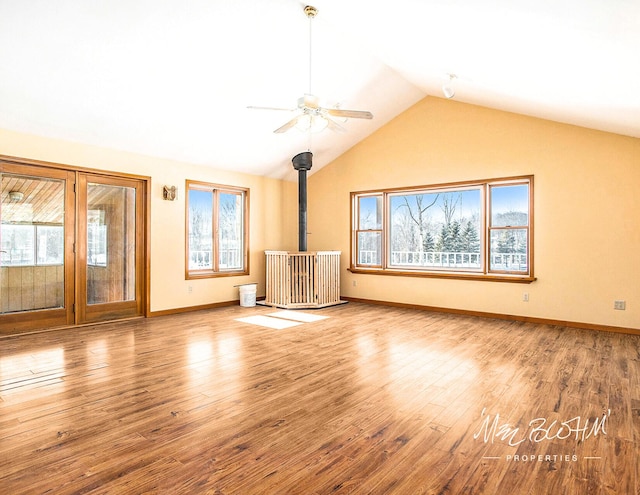 unfurnished living room with vaulted ceiling, a wood stove, hardwood / wood-style floors, and ceiling fan