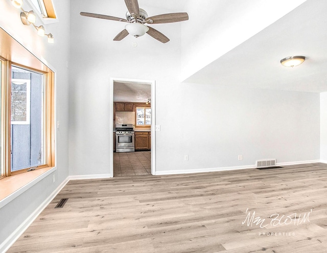 unfurnished living room featuring light hardwood / wood-style flooring, ceiling fan, and a high ceiling