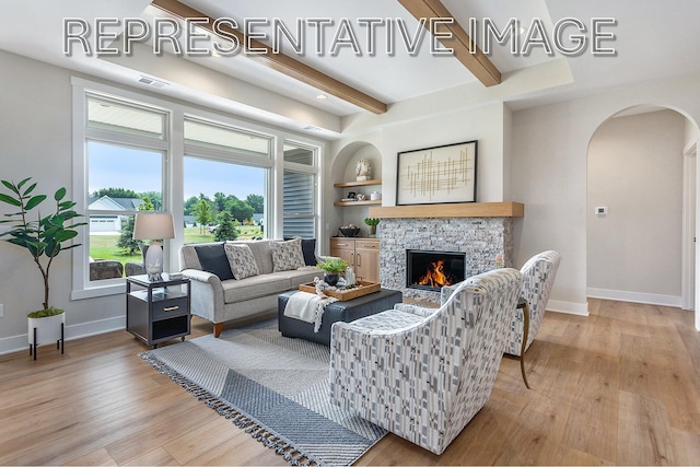 living room featuring a stone fireplace, light hardwood / wood-style flooring, built in shelves, and beamed ceiling