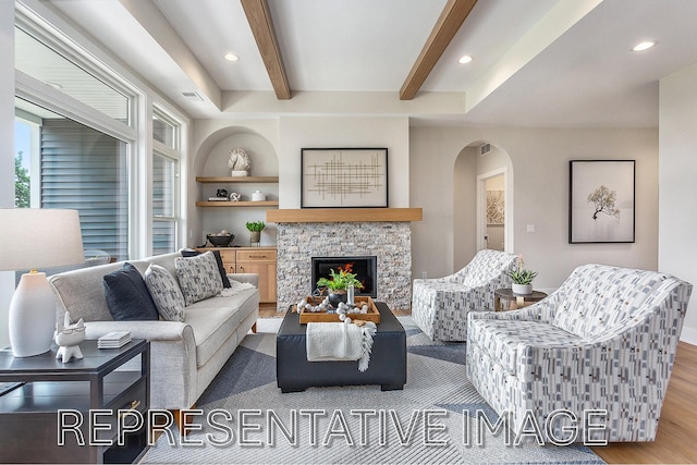 living room with beamed ceiling, a stone fireplace, and light hardwood / wood-style flooring