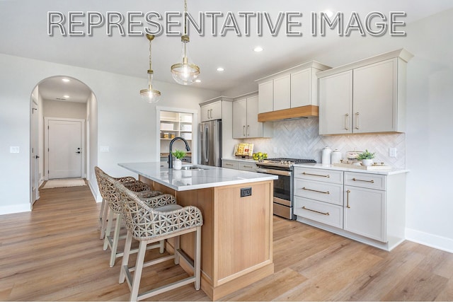 kitchen with an island with sink, sink, white cabinets, hanging light fixtures, and stainless steel appliances