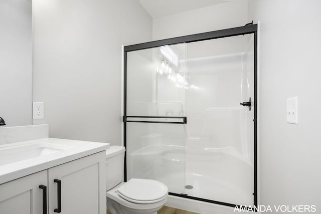 bathroom featuring a shower with door, vanity, and toilet