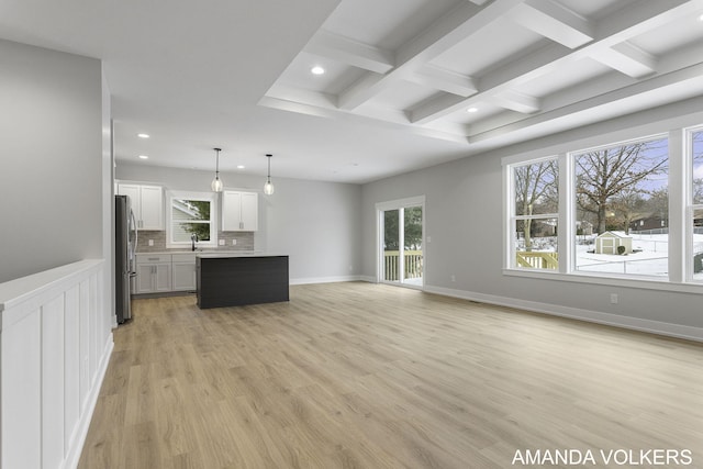 unfurnished living room featuring coffered ceiling, plenty of natural light, sink, and light hardwood / wood-style flooring