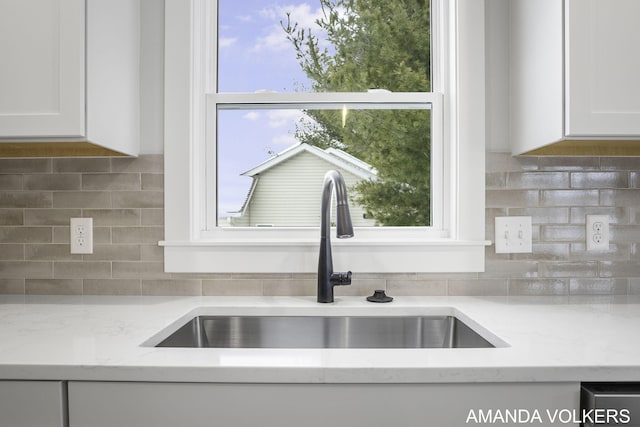 details featuring tasteful backsplash, sink, white cabinets, and light stone counters