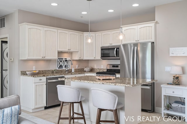 kitchen featuring stacked washing maching and dryer, appliances with stainless steel finishes, white cabinets, hanging light fixtures, and a center island