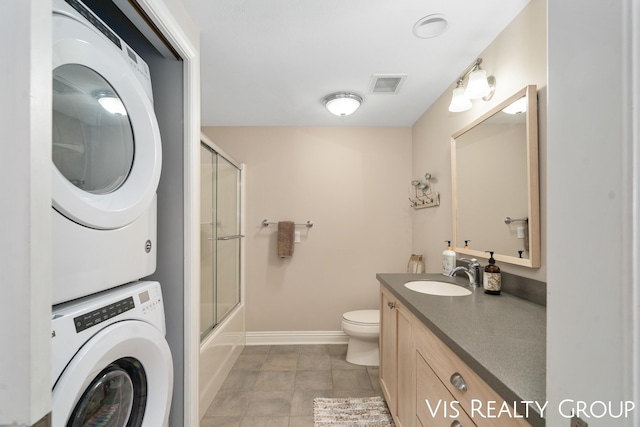 full bathroom featuring enclosed tub / shower combo, stacked washer and clothes dryer, toilet, and vanity