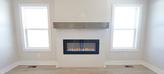 unfurnished living room with plenty of natural light, light wood-type flooring, a tile fireplace, and visible vents