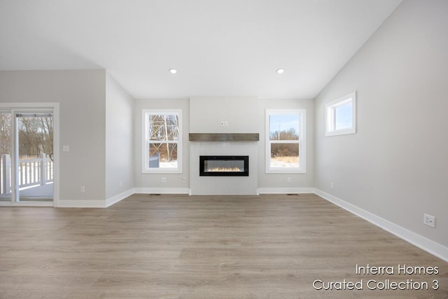 unfurnished living room featuring light wood-style floors, baseboards, and a glass covered fireplace