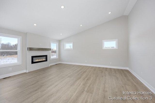 unfurnished living room featuring a glass covered fireplace, visible vents, vaulted ceiling, and light wood finished floors