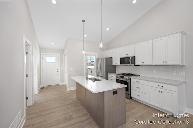 kitchen with light countertops, appliances with stainless steel finishes, a center island with sink, and white cabinets