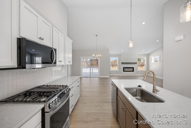 kitchen featuring stainless steel appliances, a sink, white cabinetry, open floor plan, and hanging light fixtures