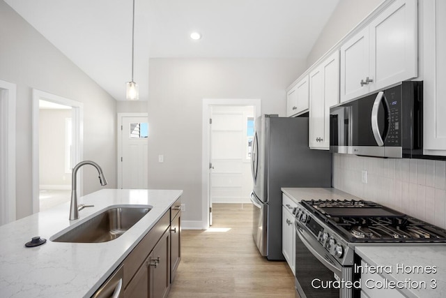 kitchen featuring a sink, white cabinets, appliances with stainless steel finishes, light stone countertops, and pendant lighting