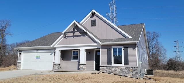 view of front of house featuring cooling unit, roof with shingles, an attached garage, concrete driveway, and stone siding