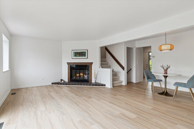 living room with stairs, wood finished floors, a tile fireplace, and baseboards