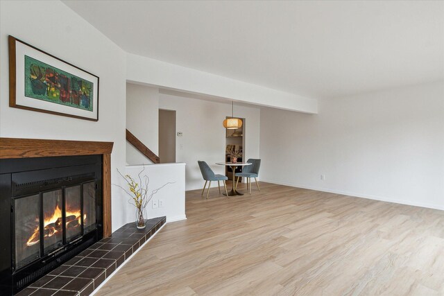unfurnished living room with wood finished floors, a tile fireplace, and baseboards