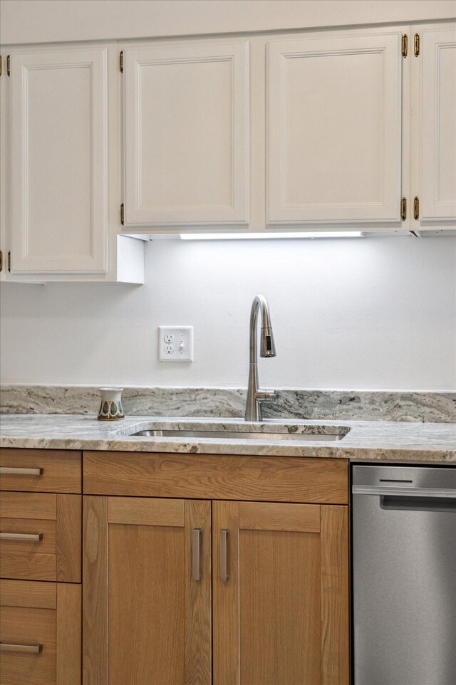 kitchen with stainless steel dishwasher, a sink, white cabinetry, and light stone counters